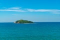 Under the blue sky and white clouds, the waves wash on the beach, and the small island in the distance