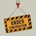 Under Construction Sign Hanging from Crane - Yellow and Black Warning Sign with Striped Border Royalty Free Stock Photo