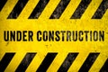 Under construction warning sign text with yellow black stripes painted over concrete wall cement facade texture background