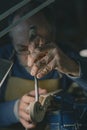 Under focused lighting in Cremona, a violin maker uses a vertical chisel to define the scroll. The scroll, blue vise, and gloved Royalty Free Stock Photo