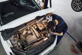 Under the hood. Man in work uniform repairs white automobile indoors. Conception of automobile service