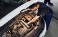 Under the hood. Man in work uniform repairs white automobile indoors. Conception of automobile service