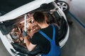 Under the hood. Man in work uniform repairs white automobile indoors. Conception of automobile service