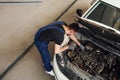 Under the hood. Man in work uniform repairs white automobile indoors. Conception of automobile service
