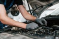 Under the hood. Man in work uniform repairs white automobile indoors. Conception of automobile service