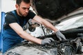 Under the hood. Man in work uniform repairs white automobile indoors. Conception of automobile service