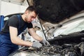 Under the hood. Man in work uniform repairs white automobile indoors. Conception of automobile service