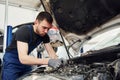 Under the hood. Man in work uniform repairs white automobile indoors. Conception of automobile service