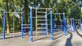 Under the trees in the paved area of the city park are a variety of metal exercise equipment for general use. Summer sunny weather