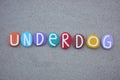 Underdog, creative text composed with multi colored stone letters over brown sand