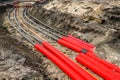 Underground electrical cable installation with red conduits laid in a trench at a construction site Royalty Free Stock Photo