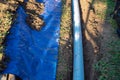 Underground PVC pipe buried in the trench installation, blue tarp with dirt, clay soils, rainwater drainage system connected to
