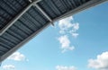 Underside view of metal shed eaves, ceiling structure against clear blue sky with scattered white clouds. Sunlight illuminates Royalty Free Stock Photo