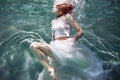 Underwater girl. Beautiful red-haired woman in a white dress, swimming under water. Royalty Free Stock Photo