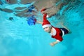 Underwater photo of a cheerful little boy in a Santa Claus costume. He dives to the bottom of the pool with a new year`s