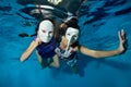 Underwater theater. Two unusual girls swim and play underwater in the pool on a blue background in white masquerade masks Royalty Free Stock Photo