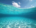 Underwater view of crystal clear ocean water with sandy seabed and sunlight patterns. Above the surface, blue sky with white Royalty Free Stock Photo