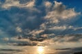 An afternoon sky with scattered clouds and a setting sun.