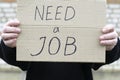Unemployed person holding a cardboard sign with a inscription need a job