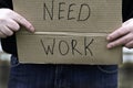 Unemployed person holding a cardboard sign with a inscription need work