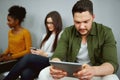 Unemployed young man sit in queue with other applicants wait for company work interview using digital tablet