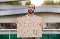 Unemployed young man wearing suit standing on street, holding Need Work placard