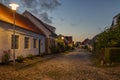 An uneven cobbled street illuminated by streetlamps and the sunset in the west