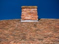 Uneven, weathered, old clay tiles and chimney on a traditional cottage roof in England, UK, taken on a sunny day with a blue sky.