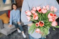 Unexpected moment in routine everyday life! Cropped photo of man\'s hands hiding holding chic bouquet of tulips behind back,