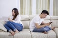 Unfaithful couple using a phone and tablet on couch