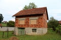 Unfinished abandoned red brick family house with closed window blinds and dilapidated wooden garage doors surrounded with uncut