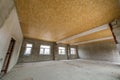 Unfinished apartment or house big loft room under reconstruction. Plywood ceiling, plastered walls, window openings, cement floor Royalty Free Stock Photo