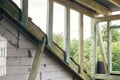 Unfinished attic wooden roof framing with vapor barrier, dormer and windows. View on timber rafters and beams on aerated concrete Royalty Free Stock Photo