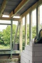 Unfinished attic wooden roof framing with vapor barrier, dormer and windows. View on timber rafters and beams on aerated concrete