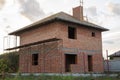 An unfinished brick house with a wooden roof frame is still under construction.