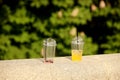 Unfinished chilled drinks in plastic disposable glasses are thrown on a stone fence in the park. Orange and strawberry juice with Royalty Free Stock Photo
