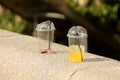 Unfinished chilled drinks in plastic disposable glasses are thrown on a stone fence in the park. Orange and strawberry juice with Royalty Free Stock Photo