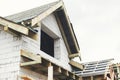 Unfinished house. Wooden roof framing with vapor barrier and dormer on block walls with windows. New modern farmhouse construction Royalty Free Stock Photo