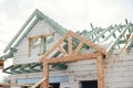 Unfinished modern farmhouse building. Wooden roof framing of mansard with dormer and aerated concrete block walls with windows.