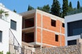 Unfinished modern red brick apartment building surrounded with new buildings and traditional stone wall with trees