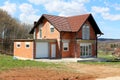 Unfinished under construction small suburban red brick family house with attached garage surrounded with grass and tall trees with Royalty Free Stock Photo
