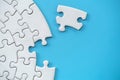 Unfinished white jigsaw puzzle on blue background with copy space. Business strategy teamwork and problem solving concept Royalty Free Stock Photo