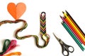 Unfinished woven friendship bracelet with skeins of thread, scissors, cut heart and selected palette of crayons colors on white ba