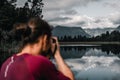 unfocused caucasian guy with long collected hair calm and relaxed taking pictures of lonely cold water lake among forest