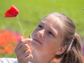 The unfocused face of a beautiful girl looking at a red poppy flower clutched in her hand in a spring sunny meadow Royalty Free Stock Photo