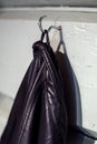 An unformal, hip black leather male jacket hanging from a robust, simple hook on a rustic, old wood wall - Concept of a
