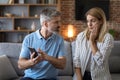 Unhappy adult caucasian man with beard shows phone to shocked lady, woman suffers from gadget addiction