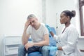 An unhappy adult man suffering from pain, severe headache, stress, ocular migraine, sits in a room and asks a doctor for Royalty Free Stock Photo