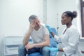 An unhappy adult man suffering from pain, severe headache, stress, ocular migraine, sits in a room and asks a doctor for Royalty Free Stock Photo