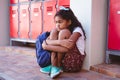 Unhappy african american schoolgirl sitting by lockers in school corridor with schoolbag Royalty Free Stock Photo